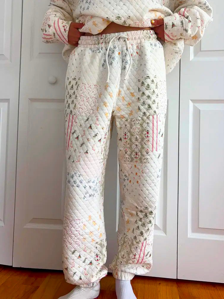 A person wearing quilted patchwork sweatpants with a matching quilted top, standing in front of white closet doors on a wooden floor.