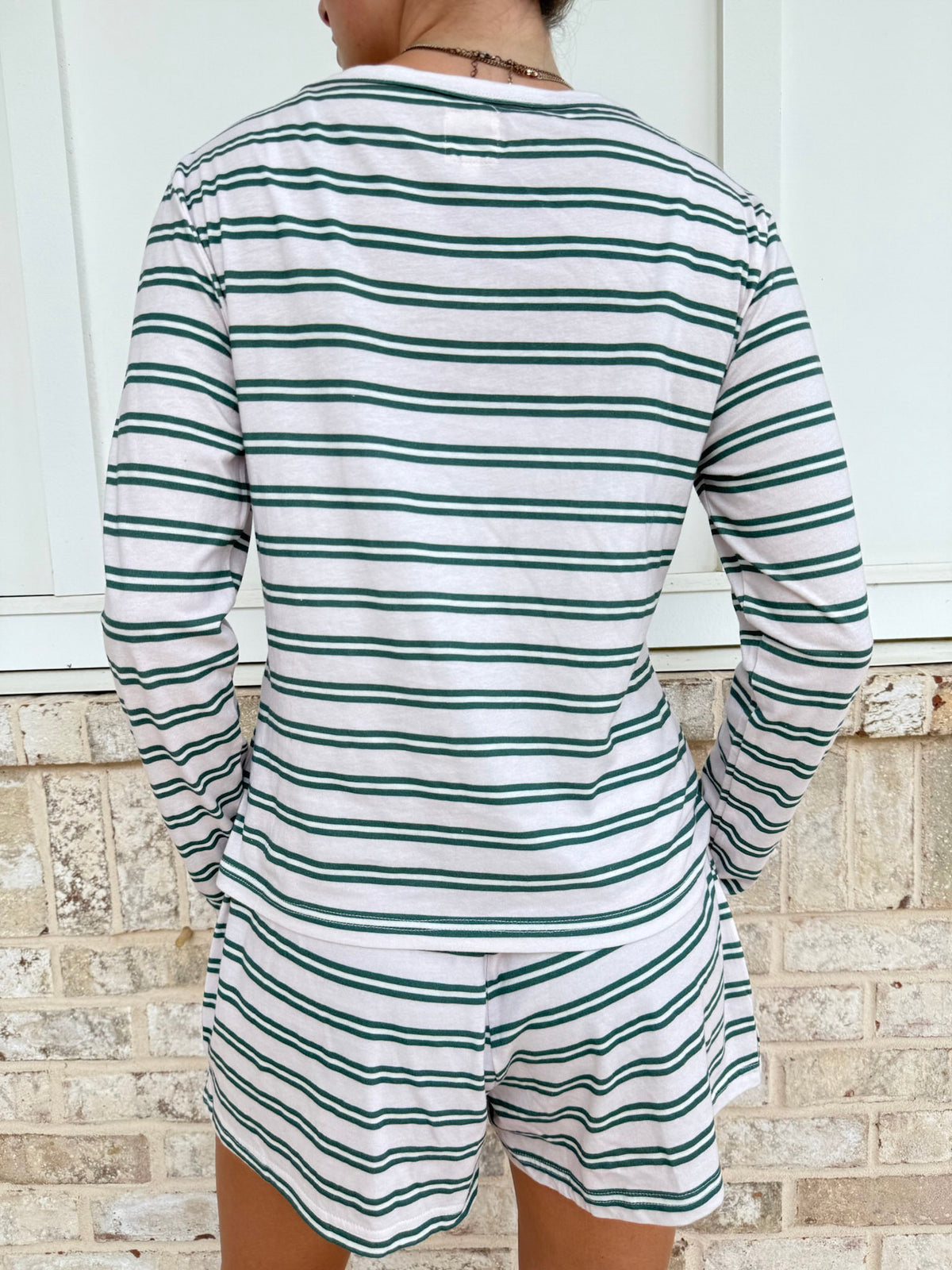 A person shown from the back wearing a matching long-sleeve top and shorts set with thin horizontal green stripes on a white base, standing against a light brick wall.