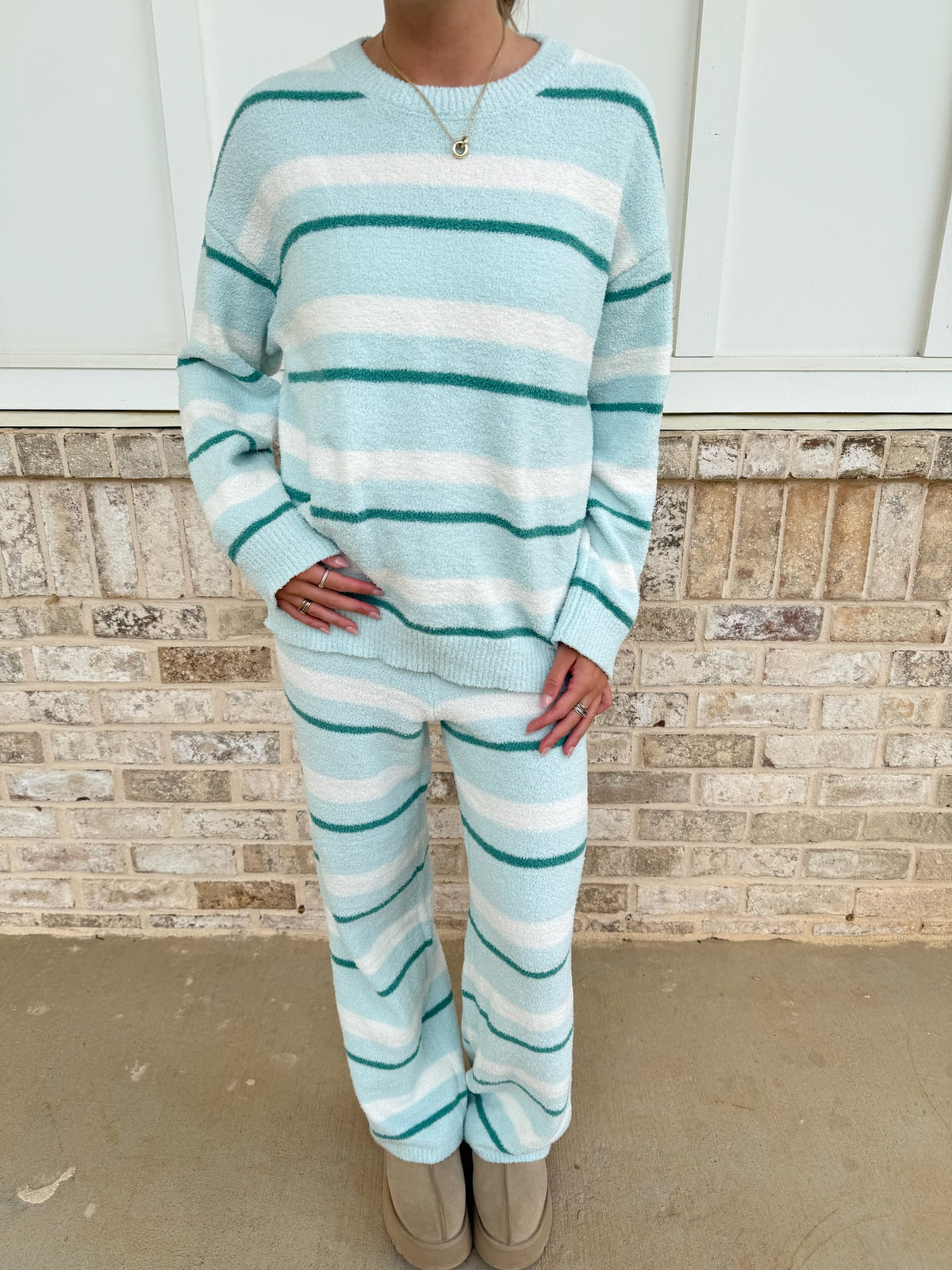 Person wearing a light blue and white striped sweater and pants set against a brick wall.