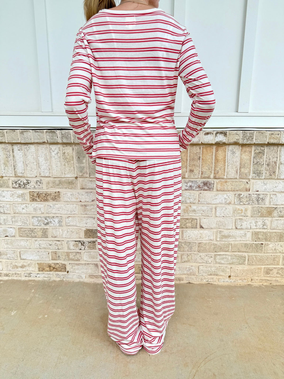 A person viewed from behind wearing a matching long-sleeve top and wide-leg pants set with red and white horizontal stripes, standing against a light brick wall.