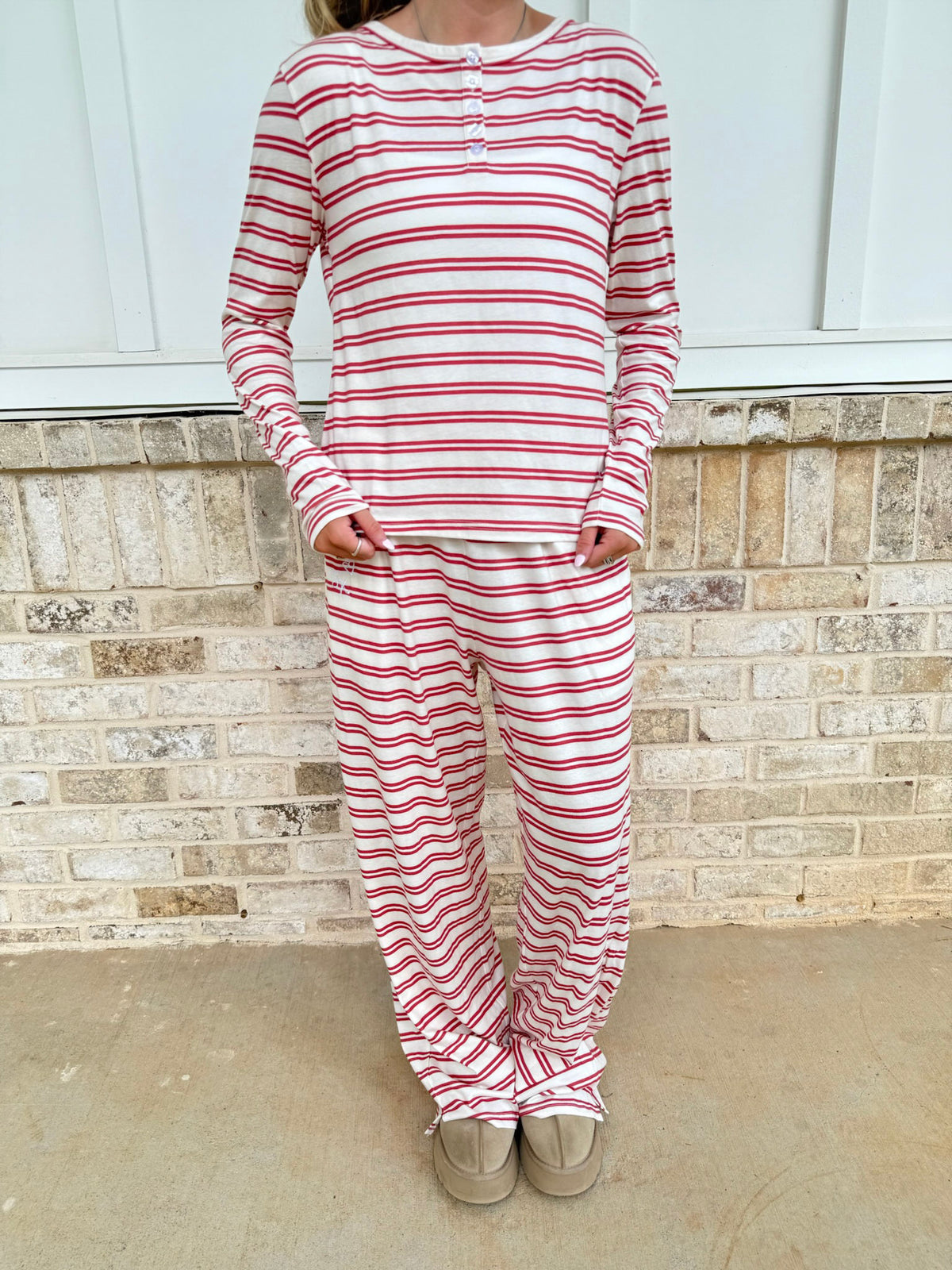 A person wearing a matching two-piece pajama set with red and white horizontal stripes, consisting of a long-sleeve henley top and matching pants, standing in front of a brick wall.