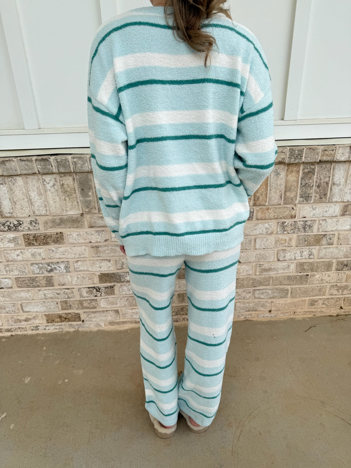 Person wearing a light blue and white striped sweater and pants in front of a brick wall.