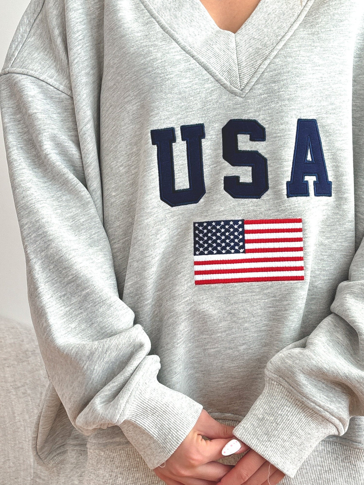Gray sweatshirt with 'USA' and American flag design worn by a person.