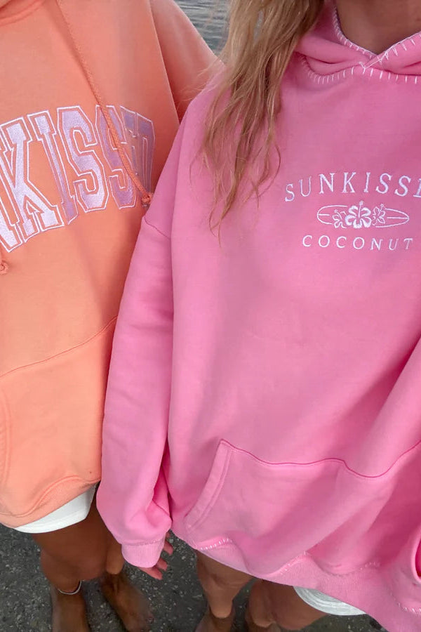 Two people wearing pink and peach hoodies with 'SUNKISSED' branding.