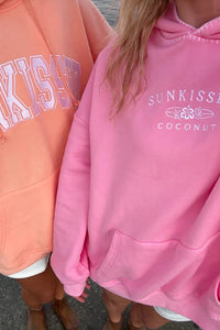 Two people wearing pink and peach hoodies with 'SUNKISSED' branding.
