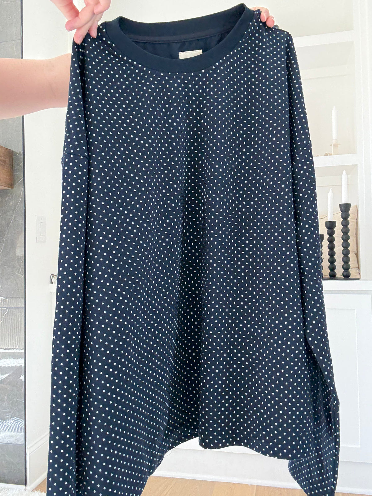 Navy blue long-sleeve shirt with white polka dots held by a person indoors.