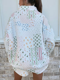 A person viewed from behind wearing a quilted white jacket with a colorful Christmas patchwork pattern, standing in front of a light-colored brick wall.