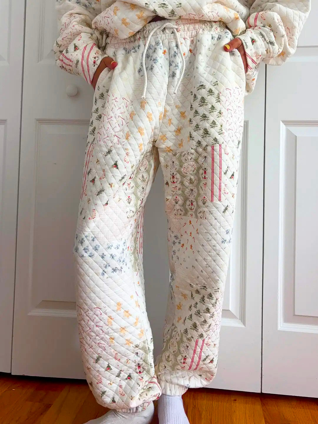 A person wearing quilted jogger-style pants with a patchwork pattern in soft pastel colors, standing in front of white paneled closet doors and a wood floor.