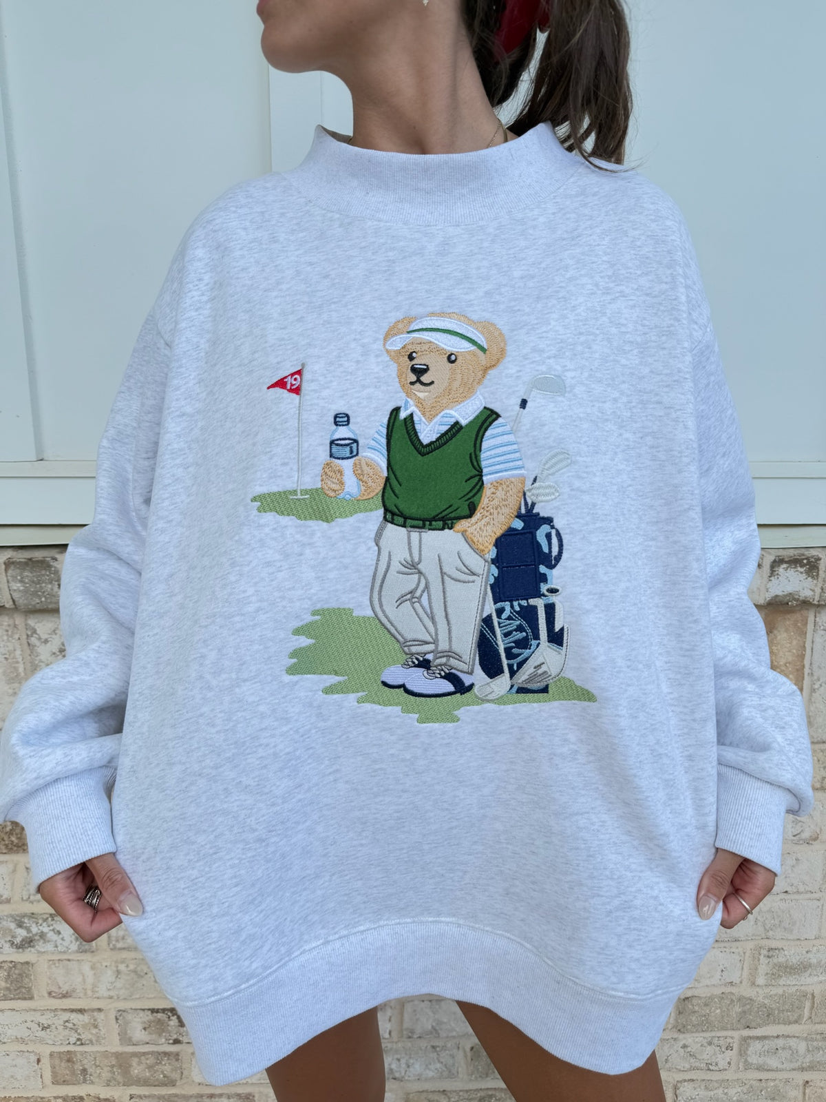 grey sweatshirt with a bear graphic playing golf on a textured wall background