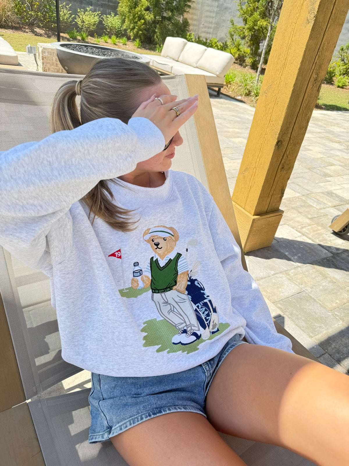 Person wearing a grey sweatshirt with a bear graphic sitting outdoors.