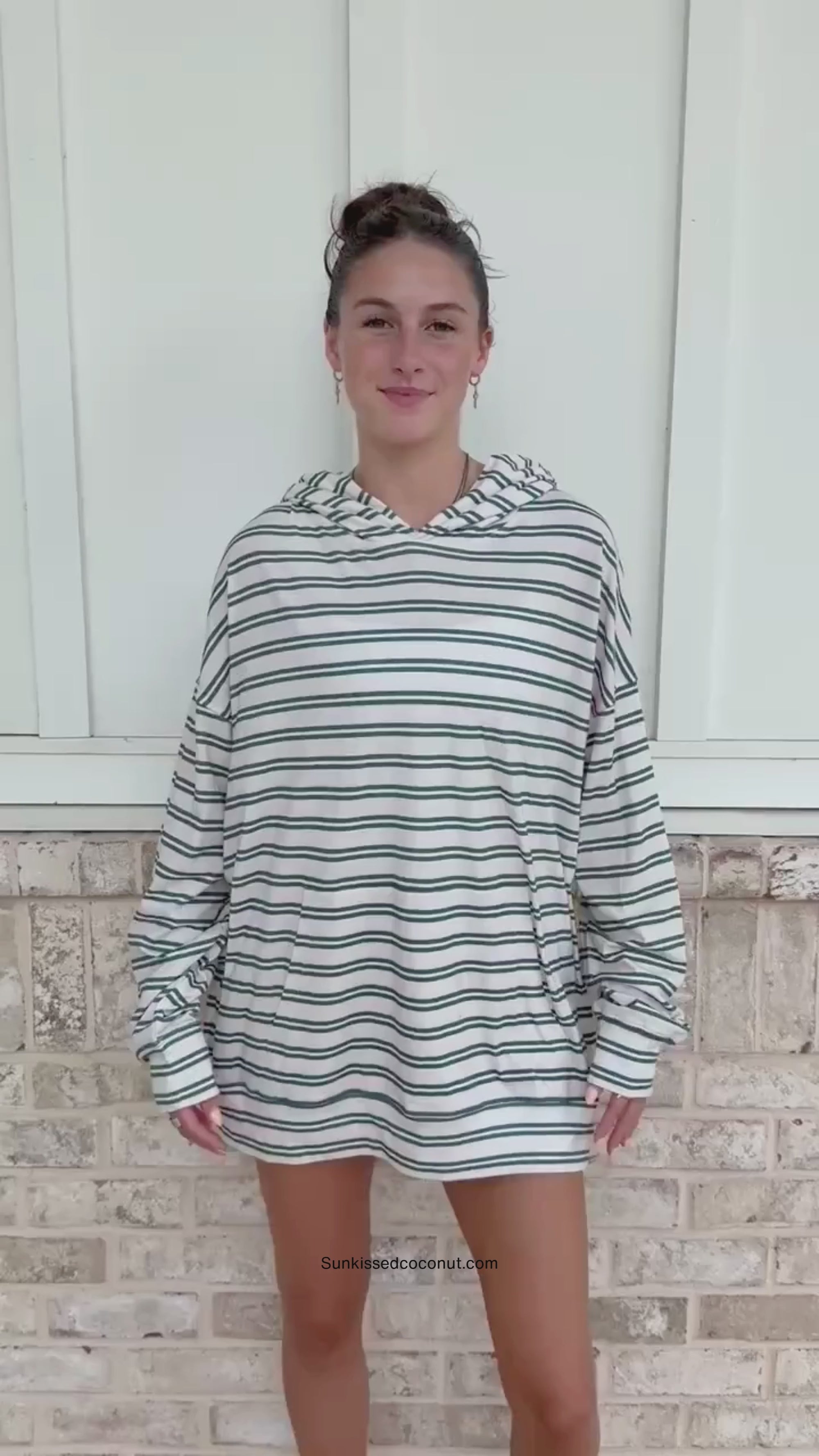 A person wearing a matching green and white striped lounge set with a hooded sweatshirt and sweatpants, standing in front of a light brick wall.