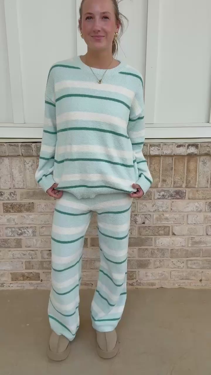Person wearing a light blue and white striped sweater and pants in front of a brick wall.